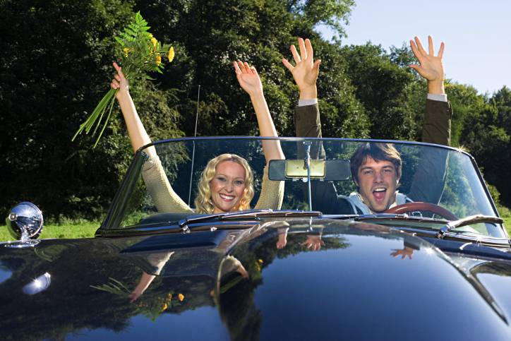 a couple raising hands inside a Jaguar E-Type convertible