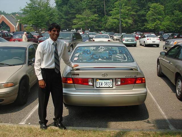 high school Sales person standing behind a car in his inventory