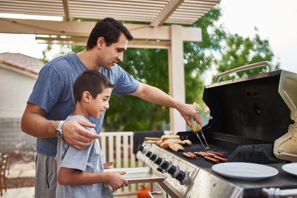 father teaching son how to grill hot dogs and bonding or grilling tips Father and son grilling barbeque